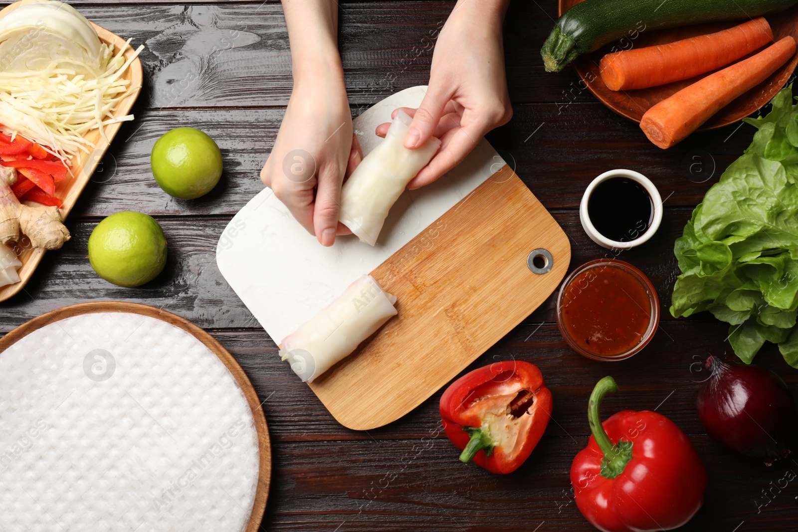 Photo of Woman making delicious spring rolls at wooden table, flat lay