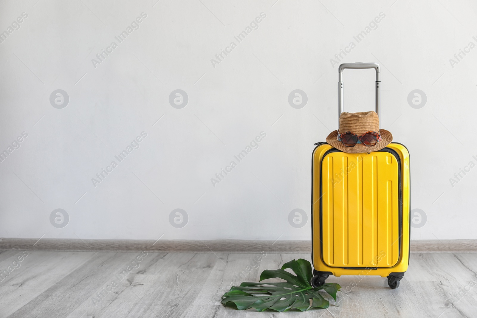 Photo of Bright yellow suitcase with hat and sunglasses near light wall indoors