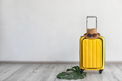 Bright yellow suitcase with hat and sunglasses near light wall indoors