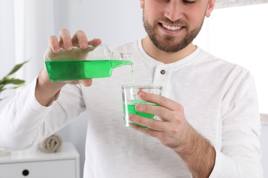 Photo of Young man with mouthwash in bathroom, closeup. Teeth and oral care