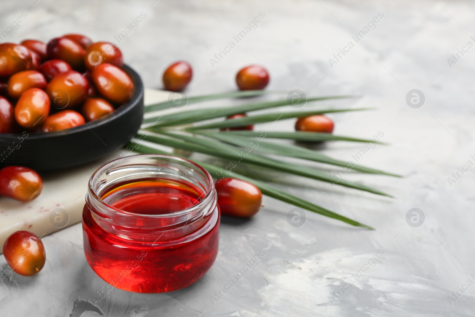 Photo of Palm oil in glass jar, tropical leaf and fruits on grey table. Space for text