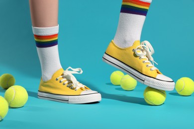 Woman posing in yellow classic old school sneakers and tennis balls on light blue background, closeup