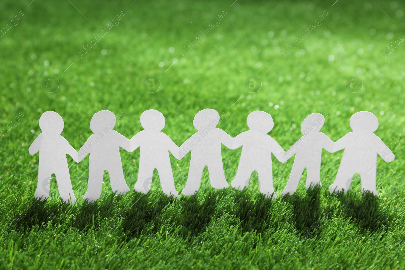 Photo of Paper people chain on green grass. Unity concept