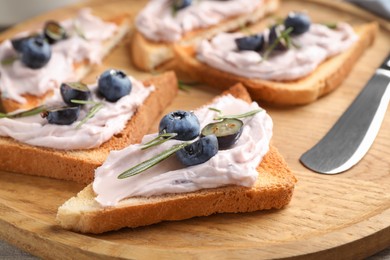 Photo of Tasty sandwiches with cream cheese, rosemary and berries on wooden tray, closeup