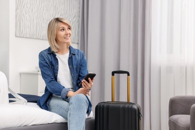 Photo of Smiling guest with smartphone relaxing on bed in stylish hotel room