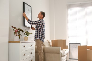 Photo of Man hanging picture on white wall in room. Interior design
