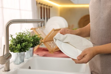 Woman wiping plate with towel in kitchen, closeup