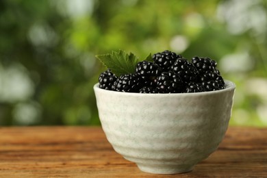 Bowl of fresh ripe blackberries on wooden table outdoors, closeup. Space for text