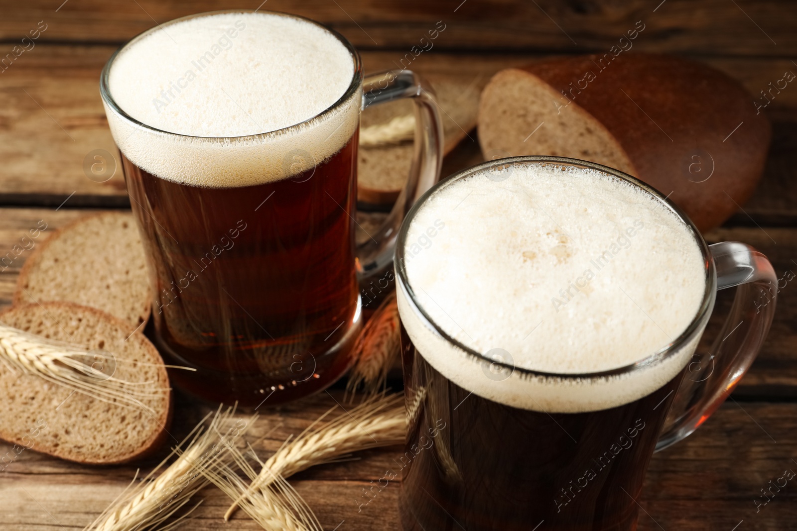 Photo of Mugs of delicious kvass, spikes and bread on wooden table