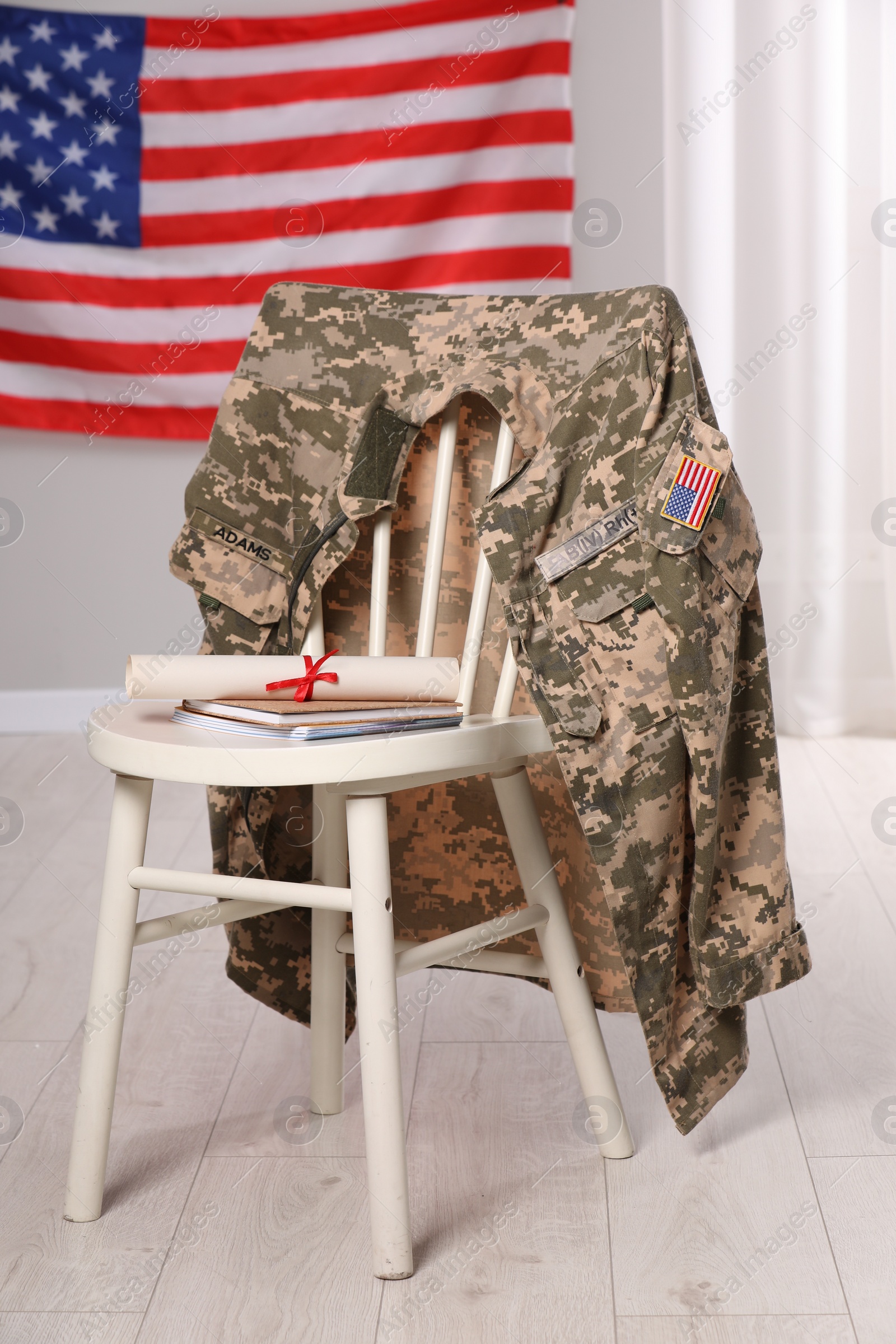 Photo of Chair with soldier uniform, notebooks and diploma near flag of United States indoors. Military education