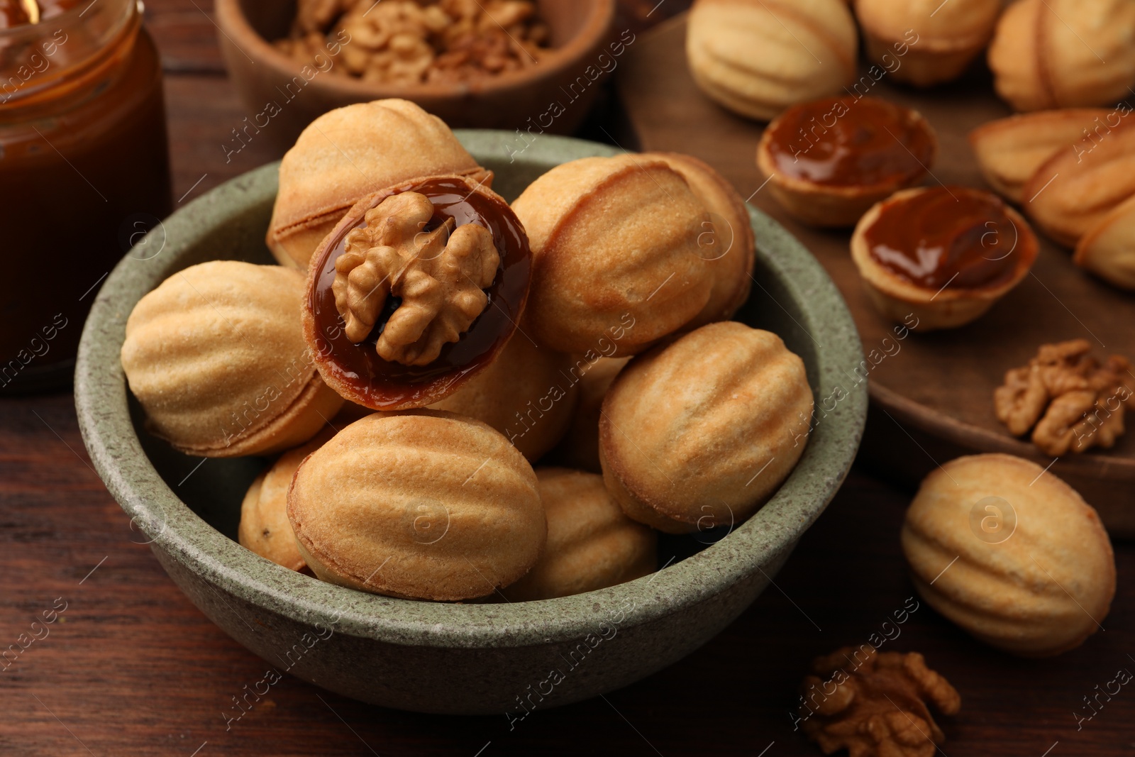 Photo of Delicious nut shaped cookies with boiled condensed milk on wooden table, closeup