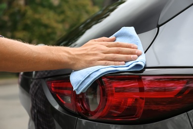 Photo of Man washing car headlight with rag outdoors, closeup