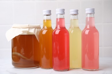 Photo of Delicious kombucha in glass bottles and jar on white marble table