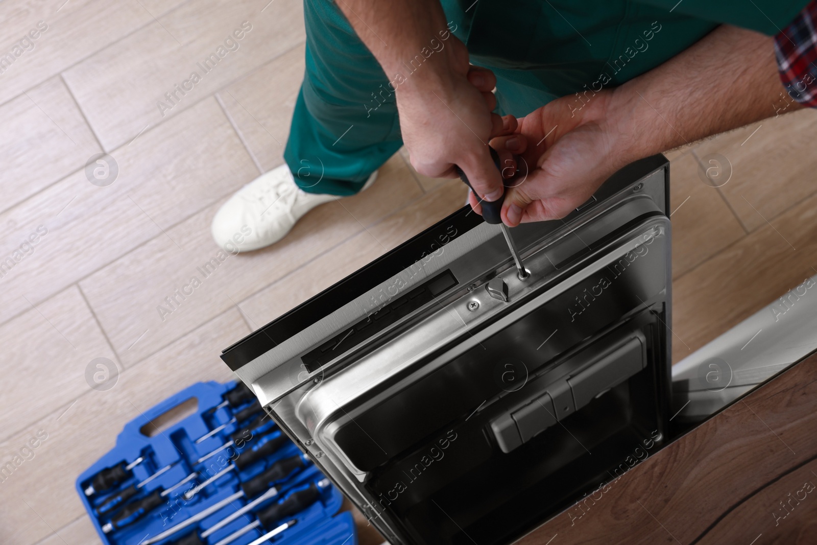 Photo of Serviceman repairing dishwasher's door with screwdriver indoors, closeup