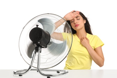 Woman suffering from heat in front of fan on white background. Summer season