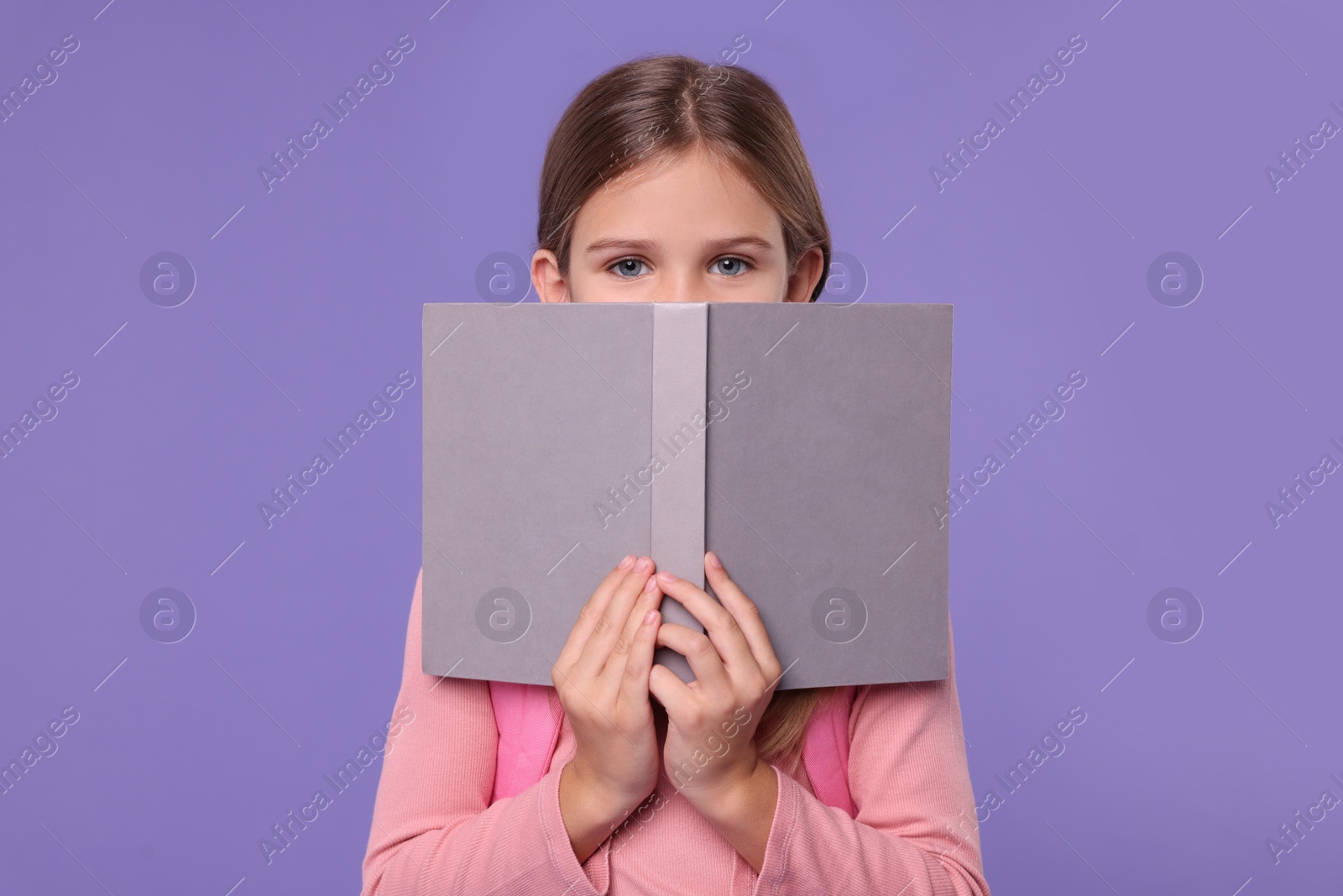 Photo of Cute schoolgirl with open book on violet background