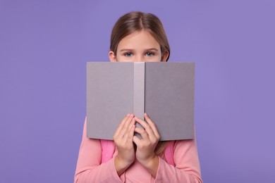 Photo of Cute schoolgirl with open book on violet background