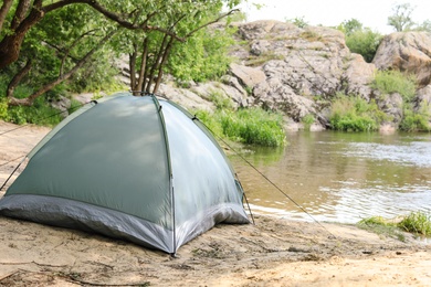 Modern camping tent on riverbank in wilderness. Space for text