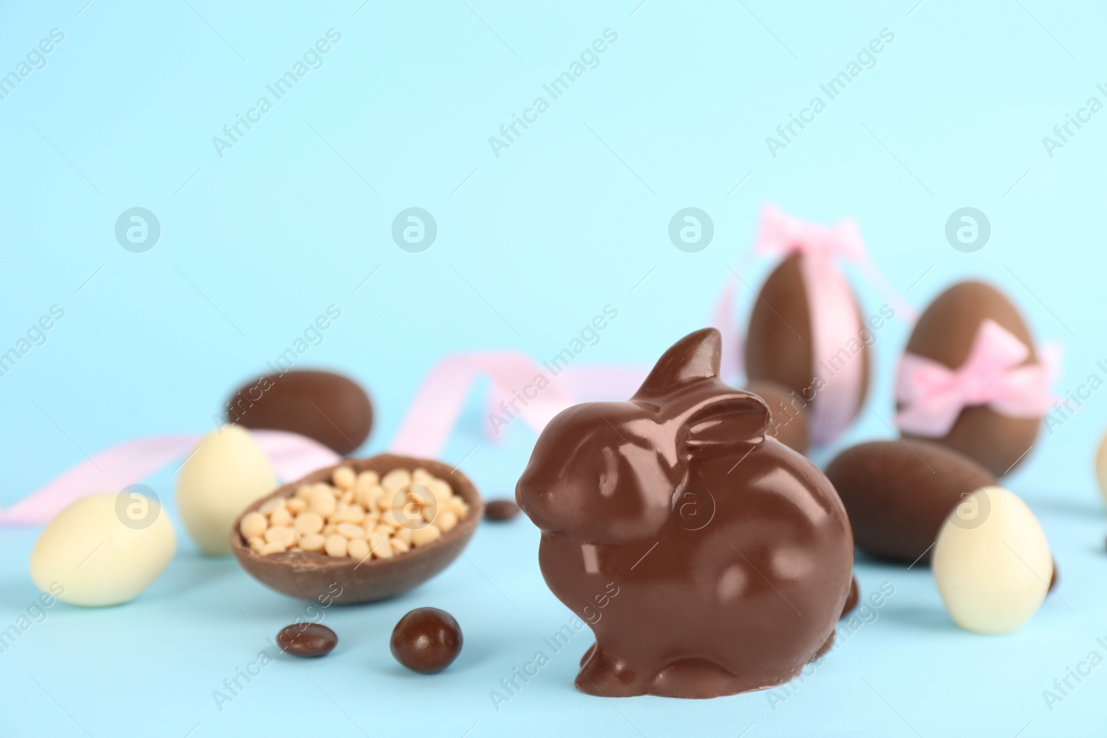 Photo of Chocolate Easter bunny, eggs and candies on light blue background. Space for text