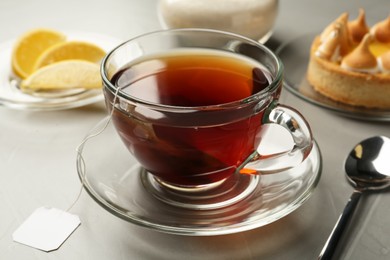 Photo of Tea bag in glass cup of hot water on grey table