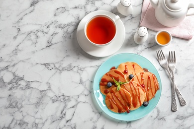 Tasty pancakes with syrup and cup of tea on table, top view