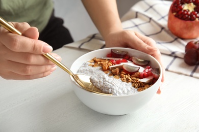 Young woman eating tasty chia seed pudding at table, closeup