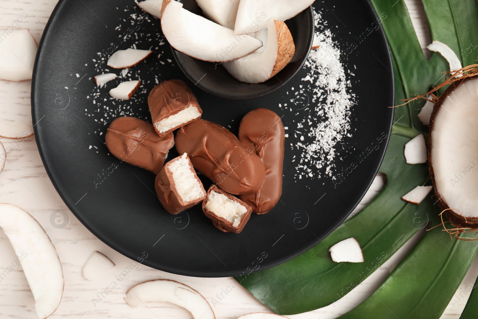 Photo of Delicious milk chocolate candy bars with coconut filling on white wooden table, flat lay