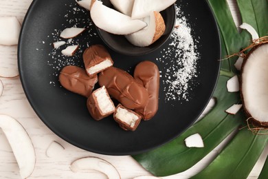 Photo of Delicious milk chocolate candy bars with coconut filling on white wooden table, flat lay