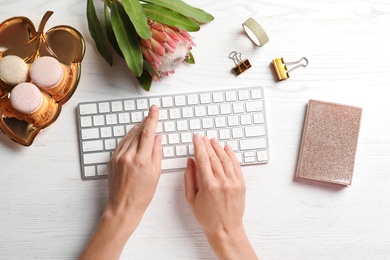 Photo of Woman using computer keyboard on wooden table decorated with tropical flower, top view. Creative design ideas