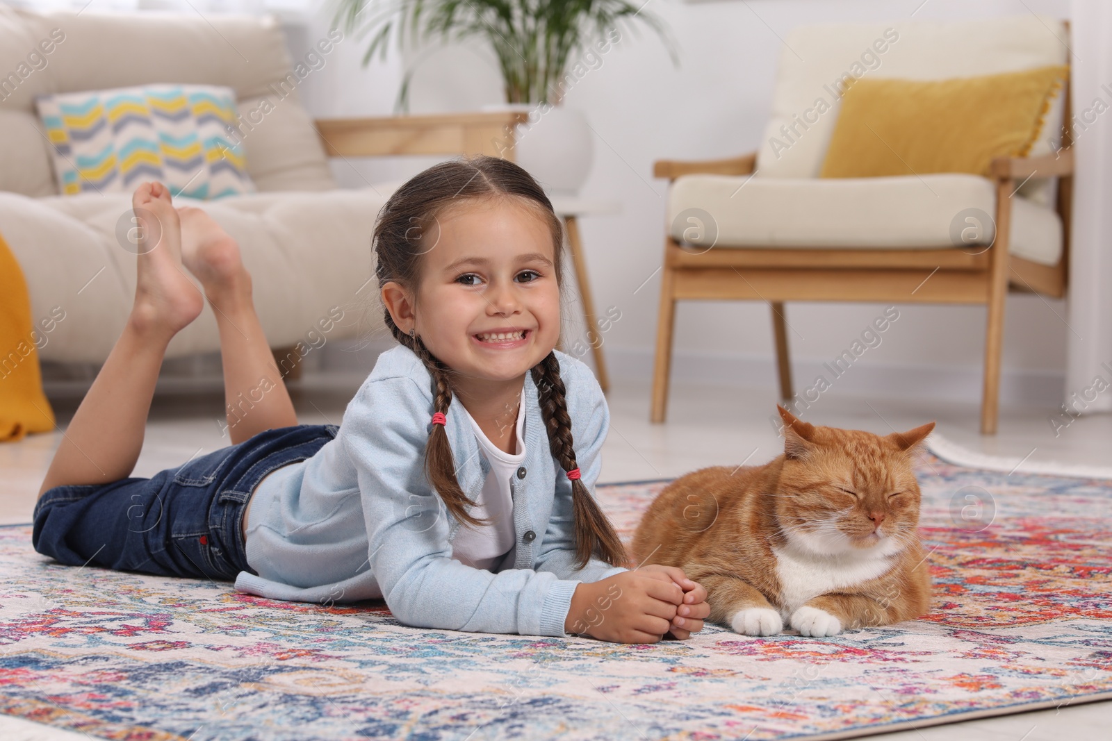 Photo of Smiling little girl and cute ginger cat on carpet at home