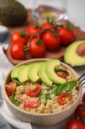 Delicious quinoa salad with tomatoes, avocado slices and spinach leaves served on table