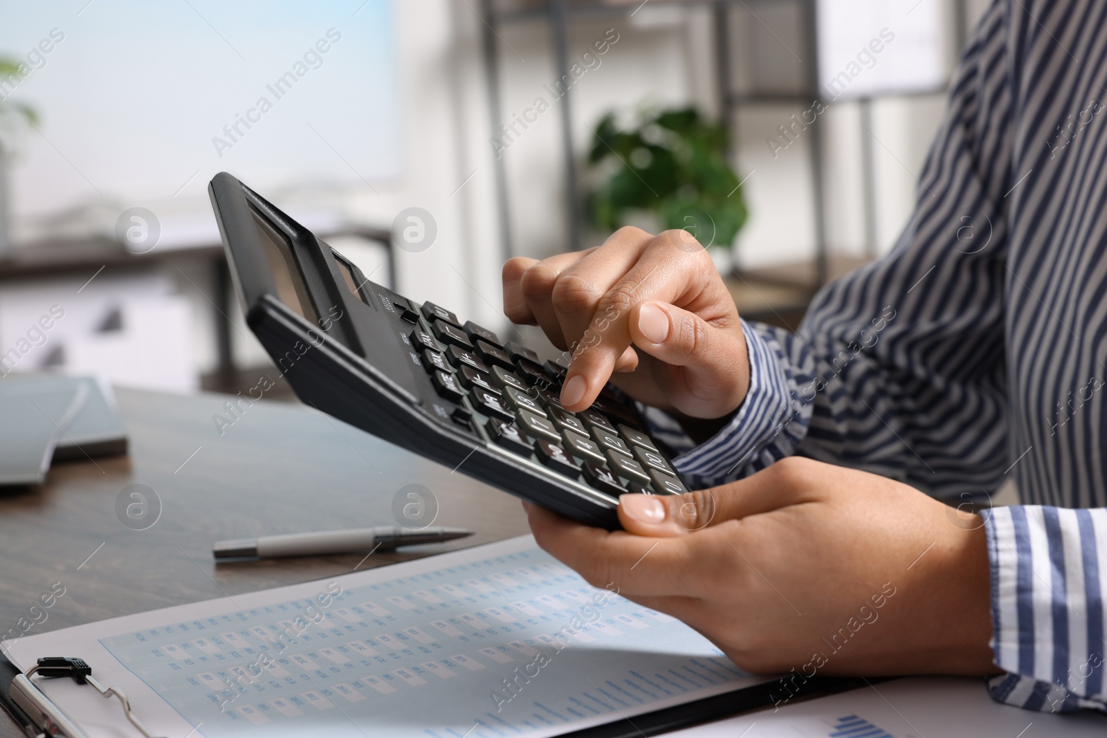 Photo of Woman using calculator at table indoors, closeup