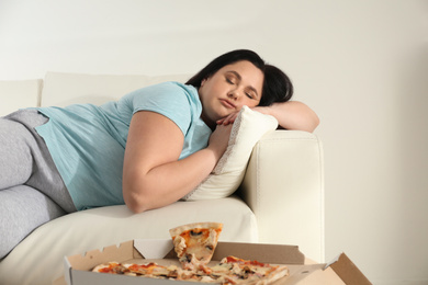Photo of Lazy overweight woman resting near pizza on table at home