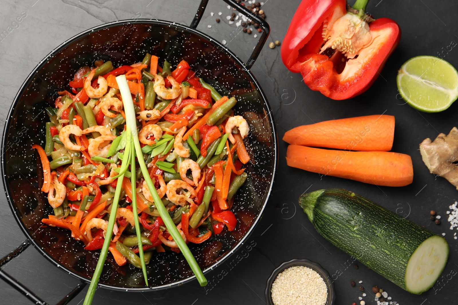 Photo of Shrimp stir fry with vegetables in wok and ingredients on black table, flat lay