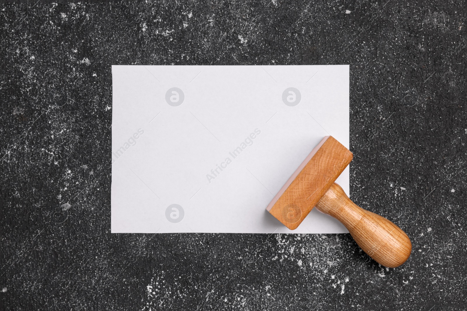 Photo of One stamp tool and sheet of paper on dark textured table, top view. Space for text