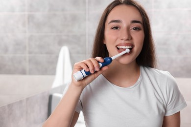 Young woman brushing her teeth with electric toothbrush in bathroom