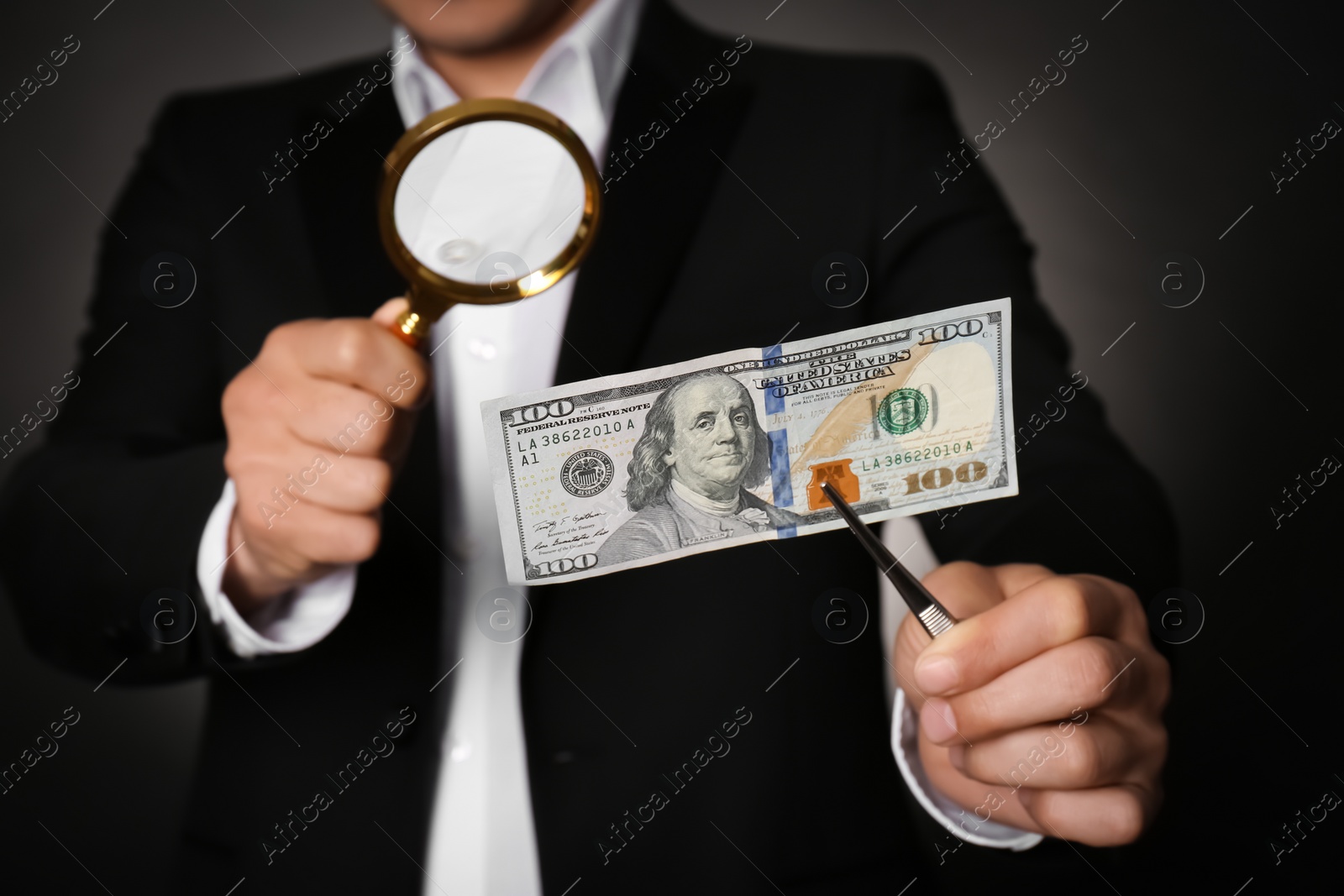 Photo of Expert authenticating 100 dollar banknote with magnifying glass against dark background, closeup. Fake money concept