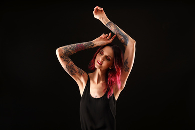 Photo of Beautiful woman with tattoos on arms against black background