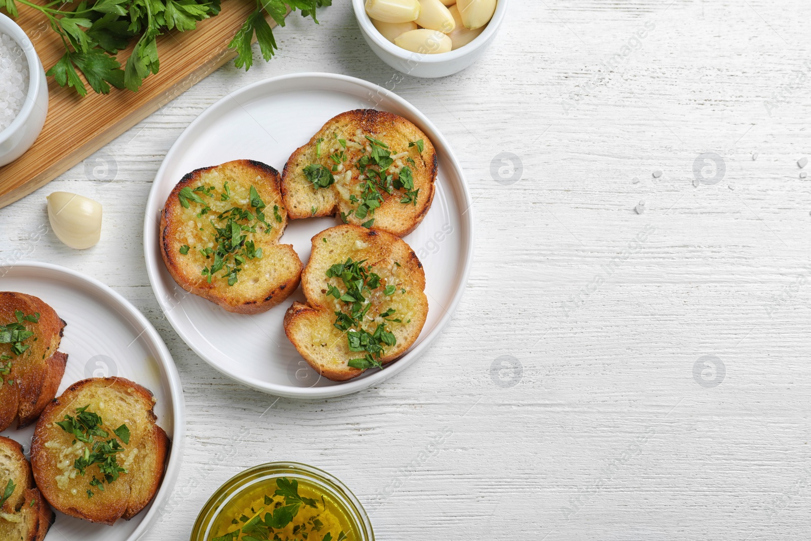 Photo of Slices of toasted bread with garlic and herb on white wooden table, flat lay. Space for text