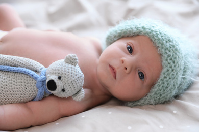 Photo of Cute newborn baby in warm hat with toy lying on bed