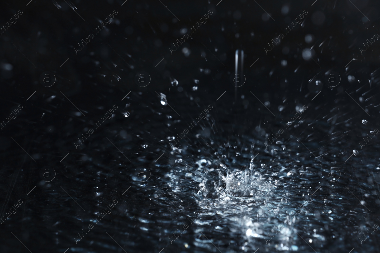 Photo of Rain drop falling down into puddle on dark background