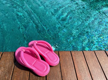 Clear rippled water in swimming pool and pink flip-flops on wooden deck outdoors. Space for text