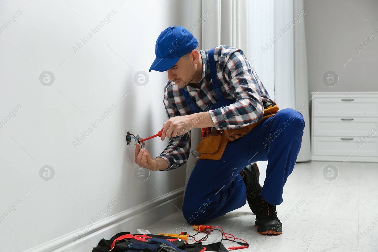 Photo of Electrician with screwdriver repairing power socket in room