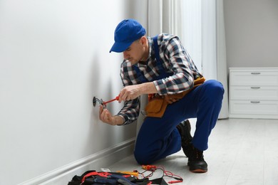 Electrician with screwdriver repairing power socket in room