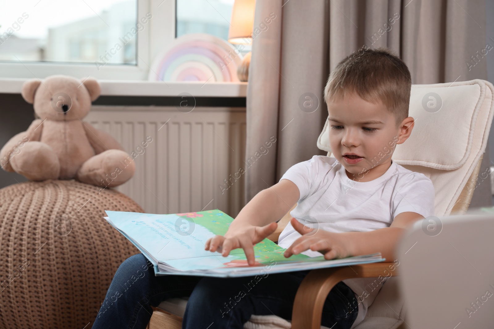 Photo of Cute little boy reading book at home, space for text
