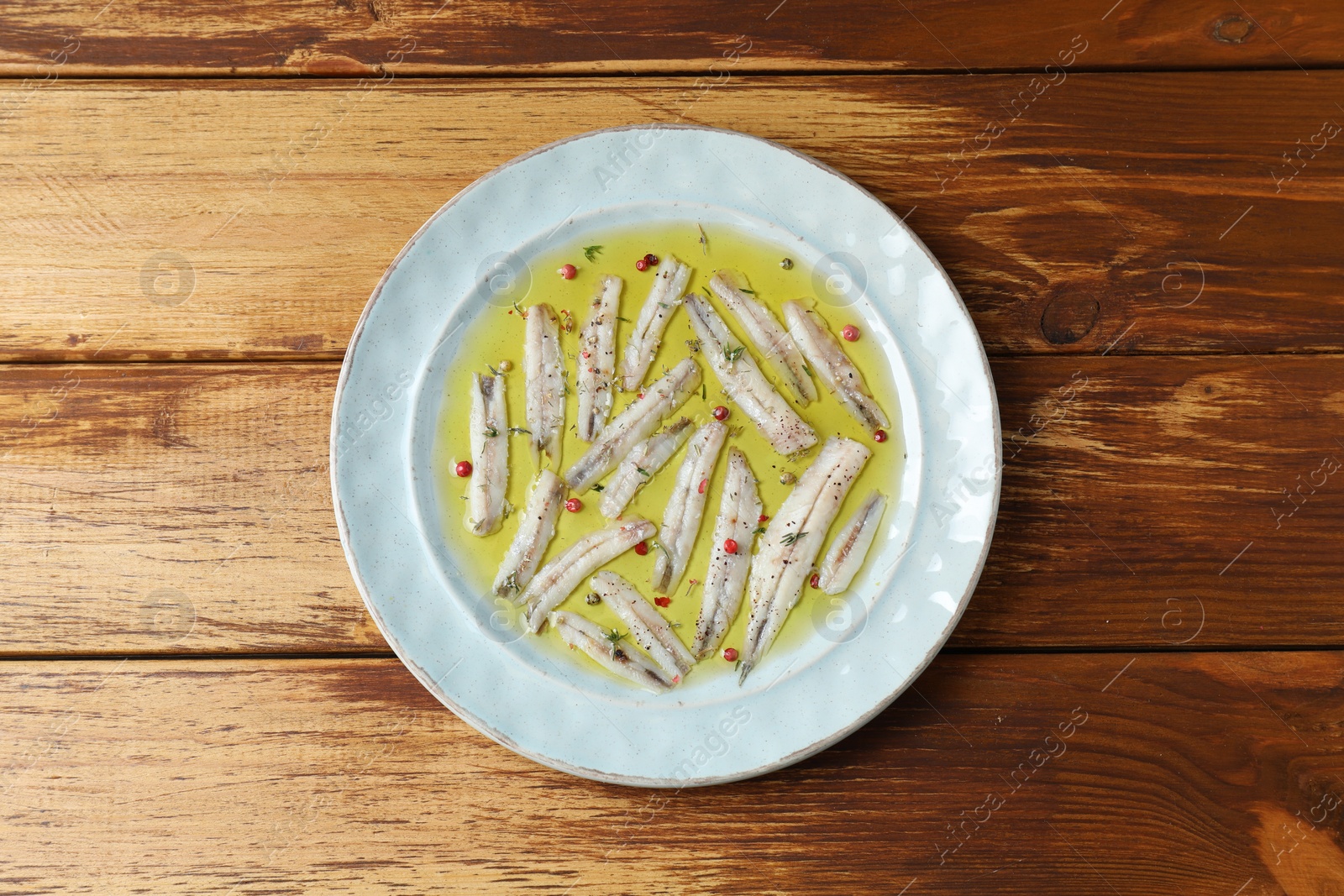 Photo of Tasty pickled anchovies with spices on wooden table, top view