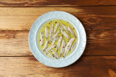 Tasty pickled anchovies with spices on wooden table, top view