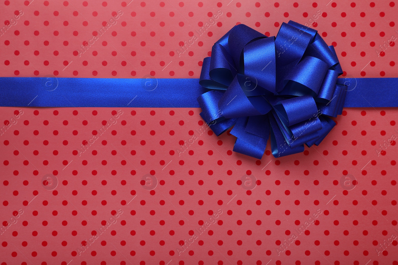 Photo of Blue ribbon with bow on red polka dot wrapping paper, top view. Space for text