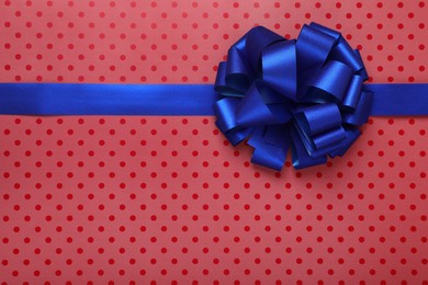 Photo of Blue ribbon with bow on red polka dot wrapping paper, top view. Space for text