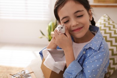 Photo of Happy little girl with cute hamster and gift box at home. Space for text